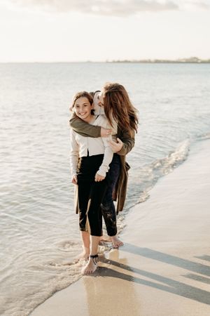 Two friends share a joyful embrace while standing in shallow ocean water at sunset on a peaceful beach.