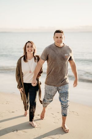 Couple walks hand in hand along peaceful beach shore at sunset.