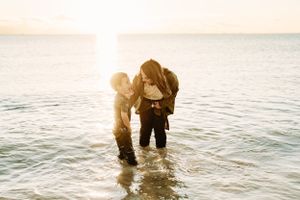 A couple stands together in shallow ocean water at sunset creating a romantic silhouette.