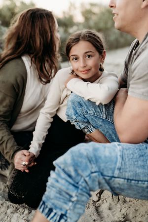 A family relaxes together on sandy ground during a casual outdoor photoshoot.