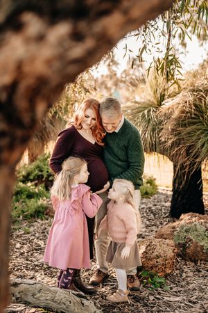 Tender maternity moment outdoors under dappled sunlight.