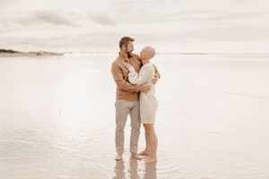 Intimate couple moment standing in shallow water at sunset on the beach.