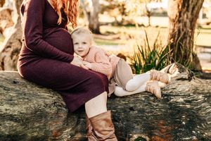 Intimate maternity portrait on a rustic fallen tree trunk with warm autumn lighting.