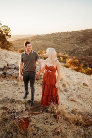 A couple walks together on a rocky hillside during sunset.