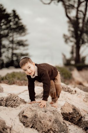 Young child in brown clothing explores rocky terrain while crawling on hands and knees.