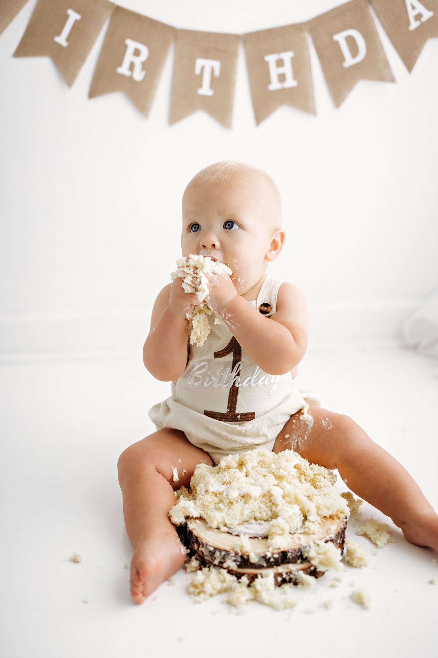Baby's first birthday cake smash photoshoot with white cake and rustic brown birthday banner decorations.
