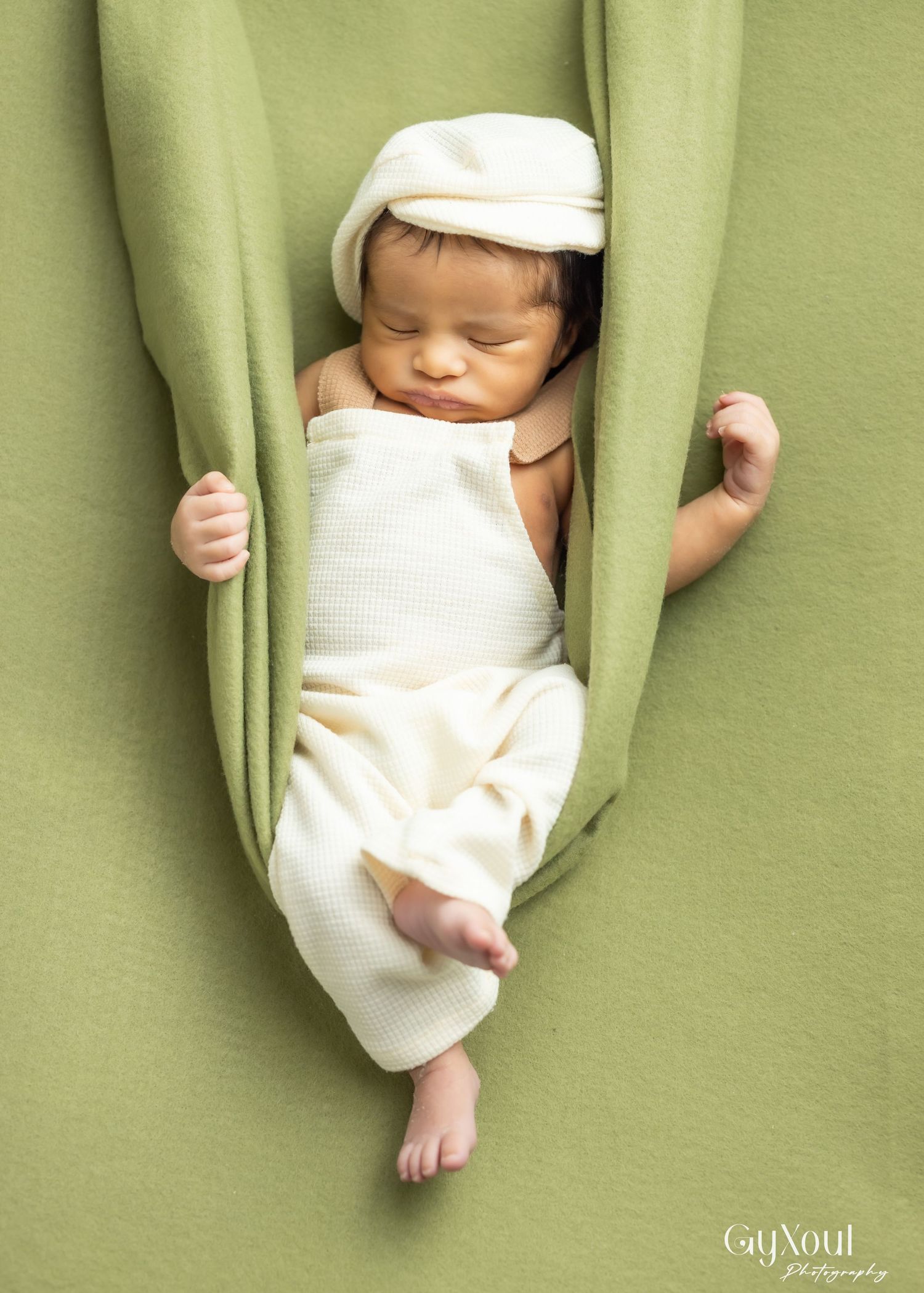 A sleeping baby wrapped in white clothes hangs peacefully between green curtains.
