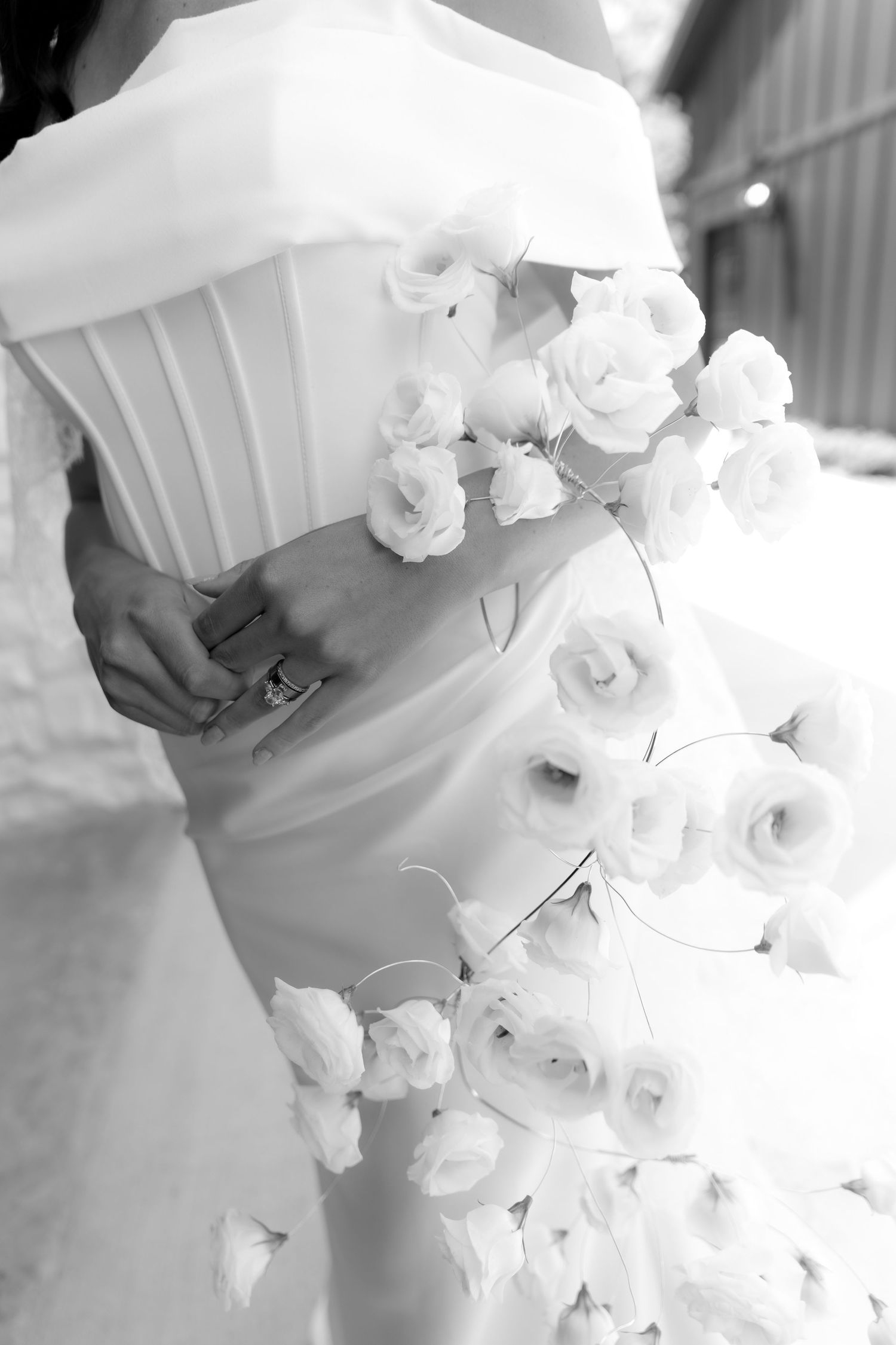 Black and white photo of a bride in a strapless wedding gown adorned with white roses at the waist.