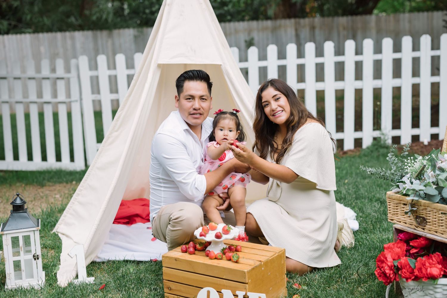 A family celebrates a milestone moment with a teepee tent, rustic decor and flowers in a backyard setting.