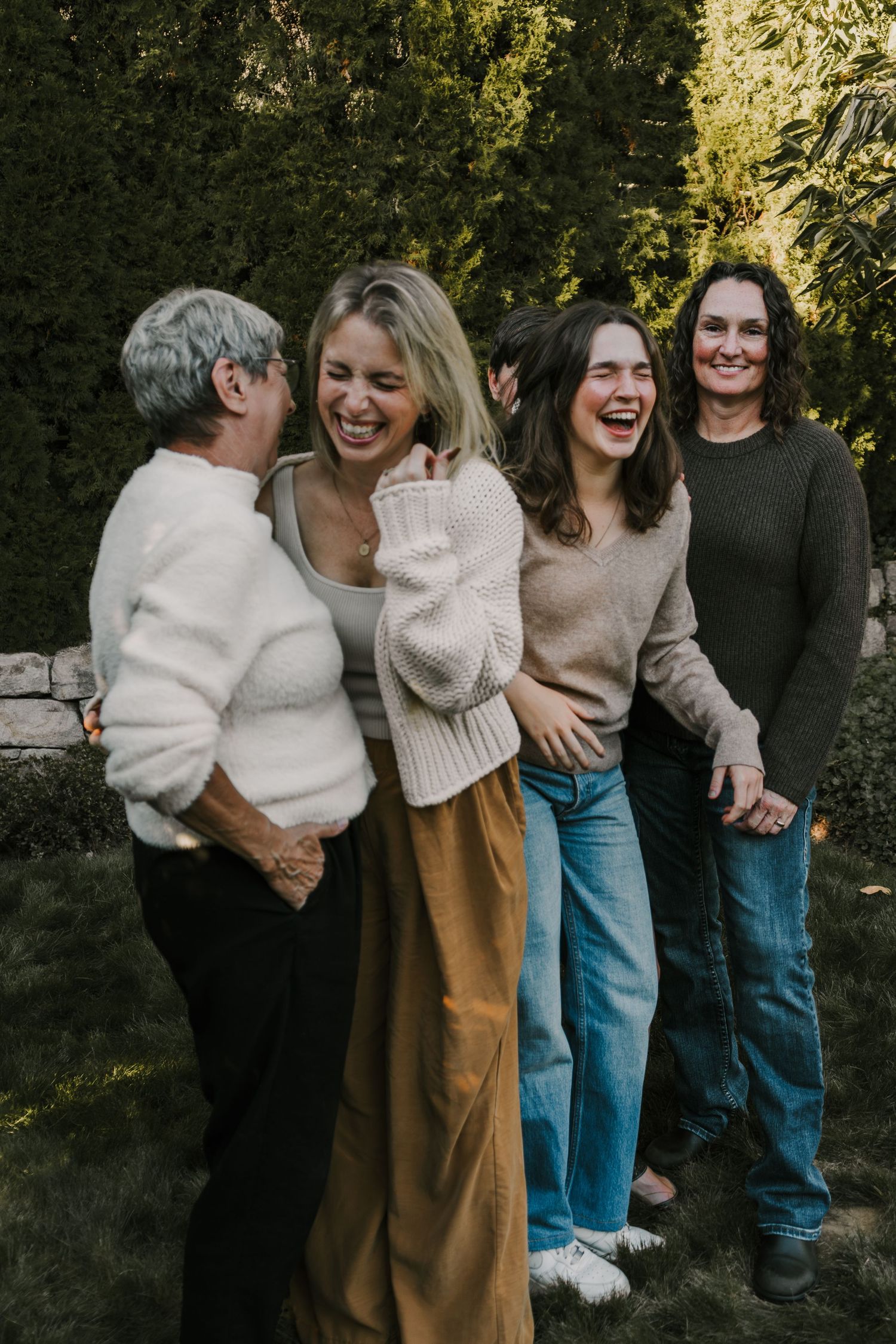 four women laughing together in a tree lined yard
