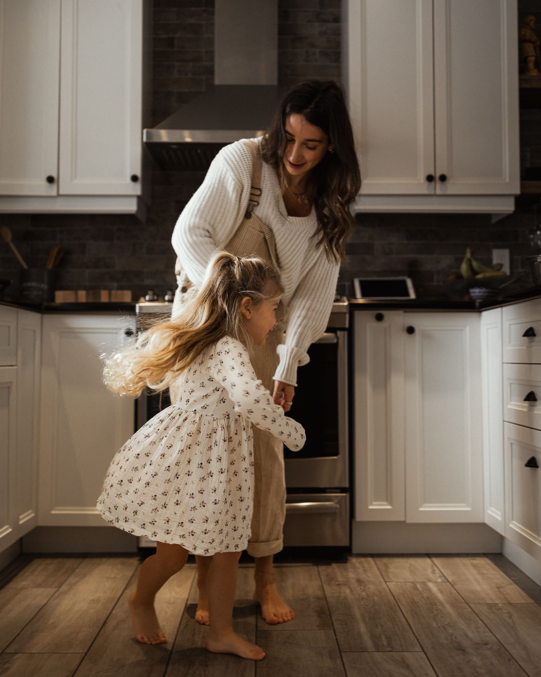 Dancing and playing together in a modern white kitchen with cozy sweaters and hardwood floors.