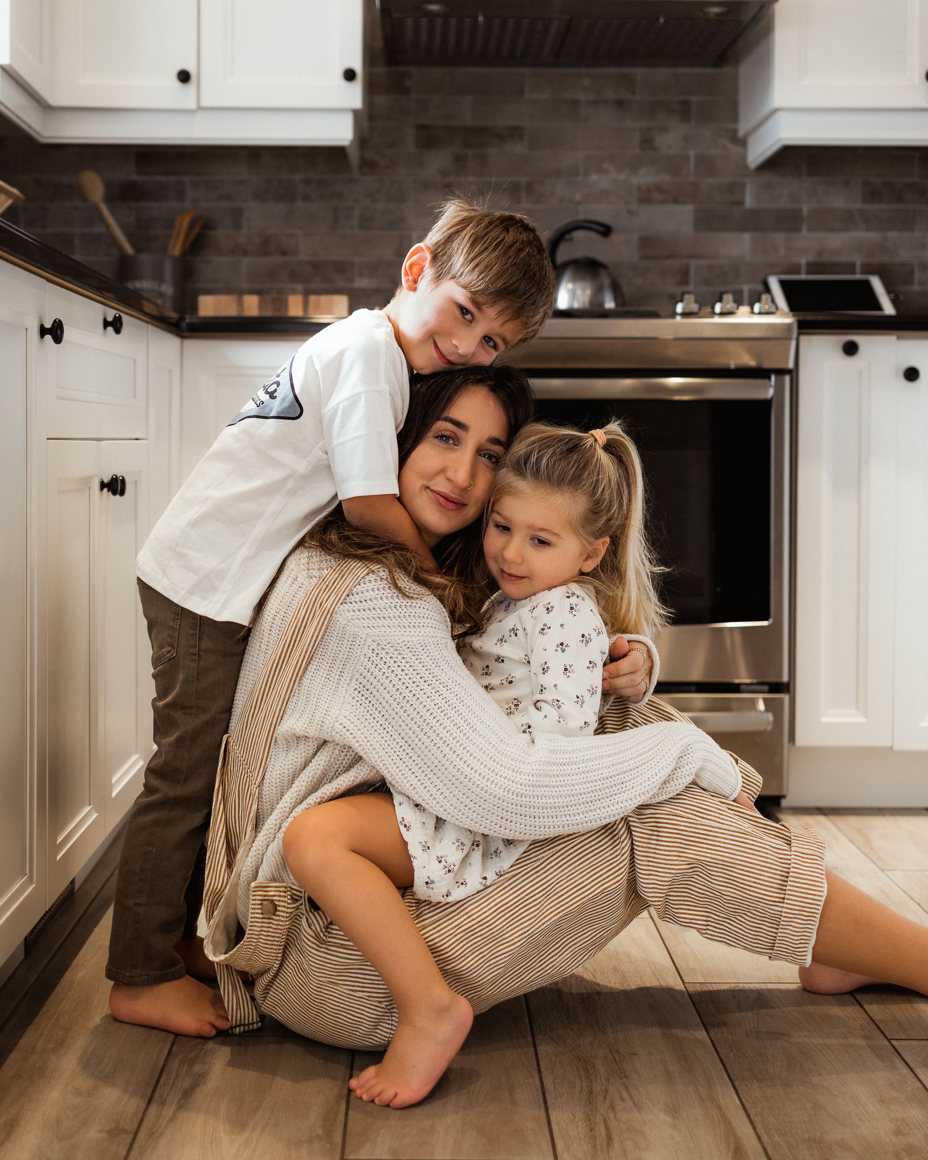 Cozy family moment on kitchen floor with white cabinets and hardwood flooring.