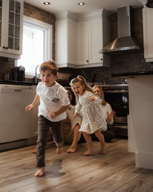 Children running and playing barefoot in modern white kitchen with hardwood floors.