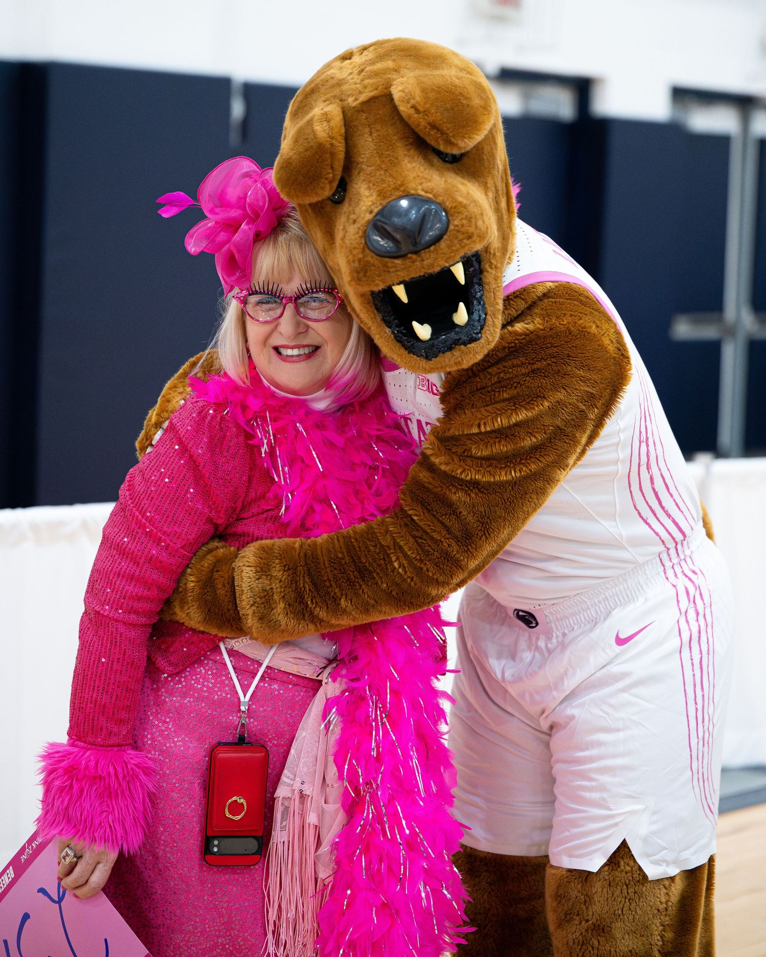 Mascot posing with attendee wearing bright pink feather boa at special event.