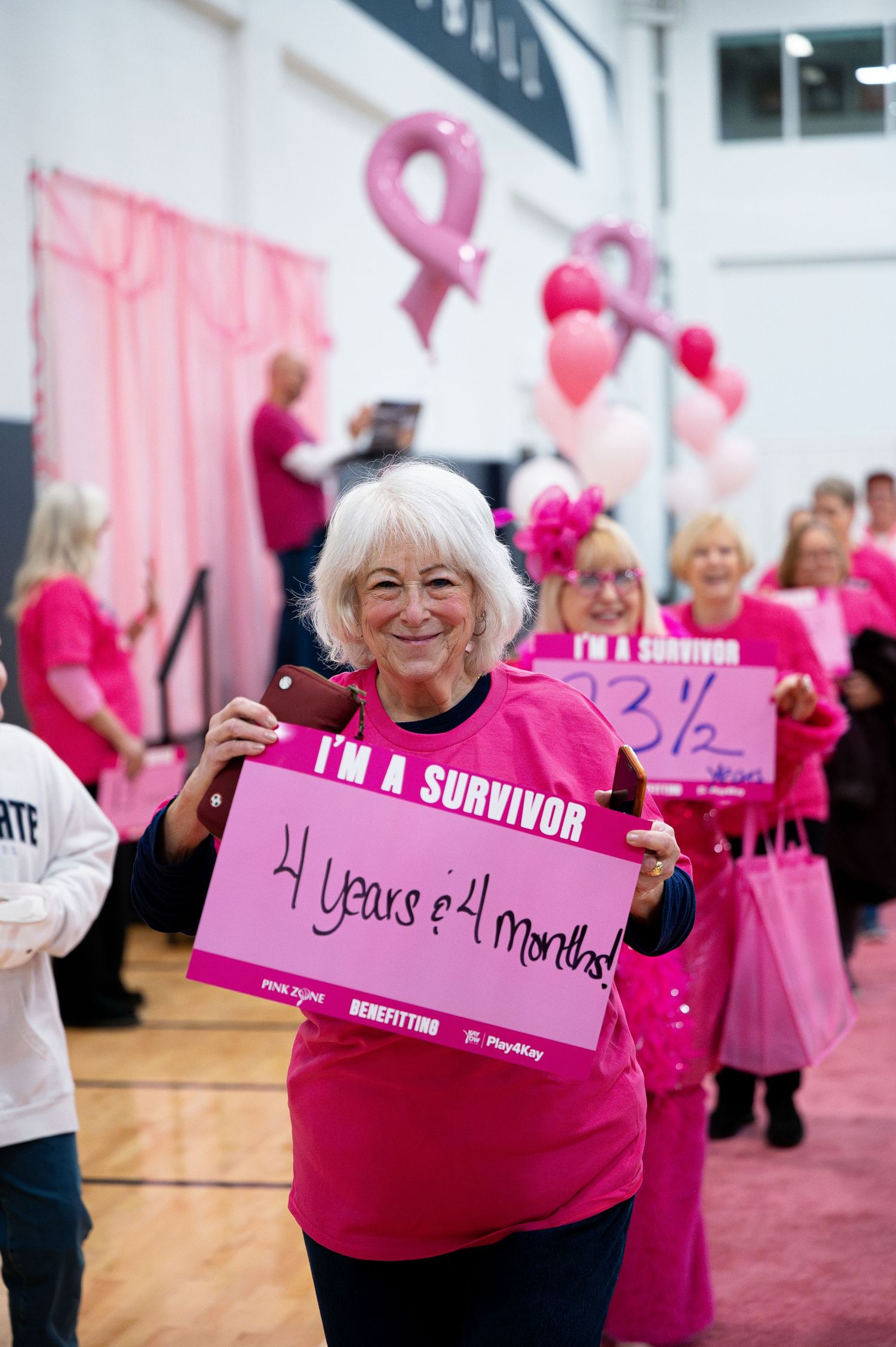 Breast cancer survivor holding pink sign showing years of survival at awareness event.