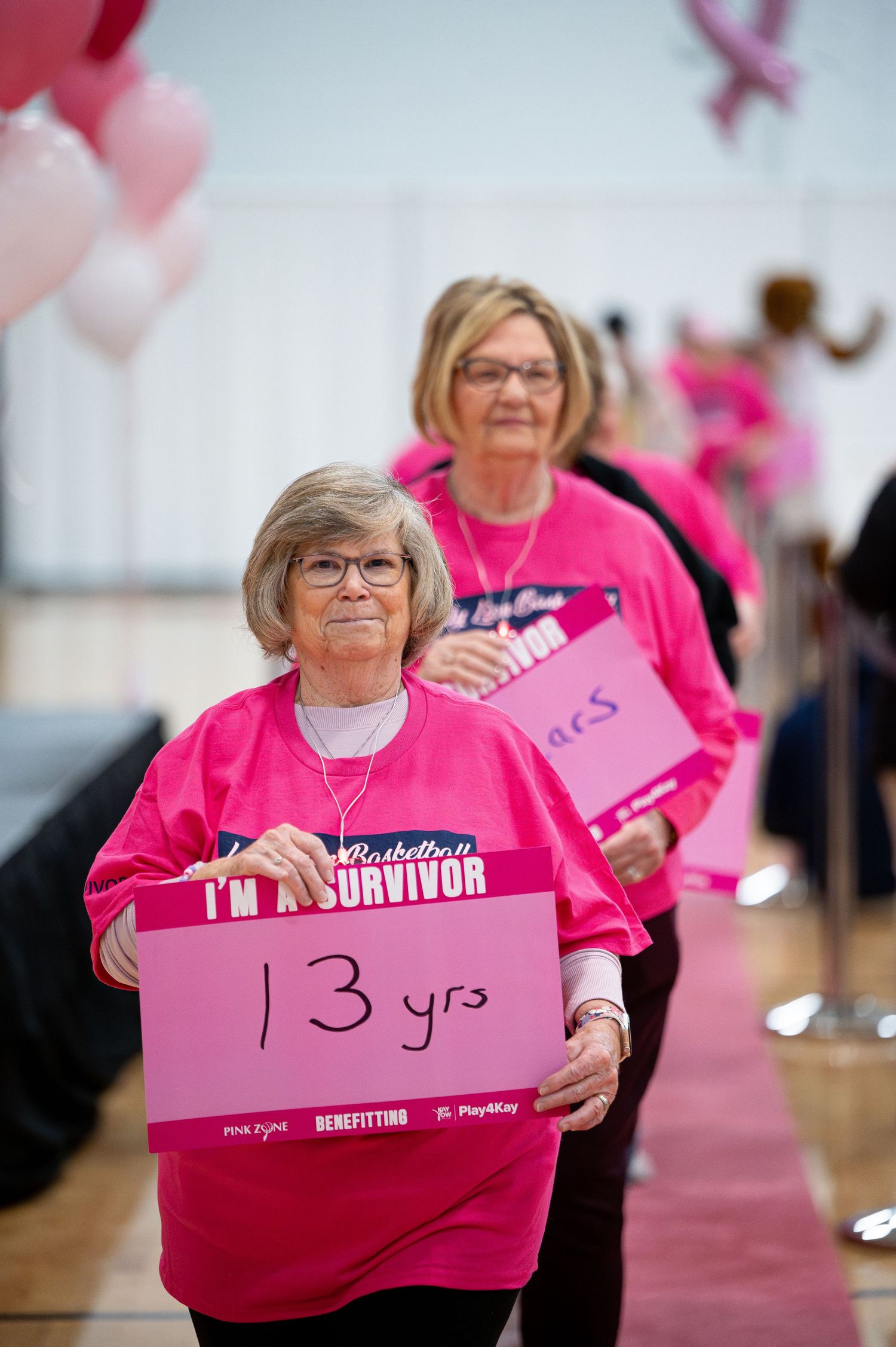 Breast cancer survivor in pink t-shirt holds sign showing 13 years of survival at celebration event.