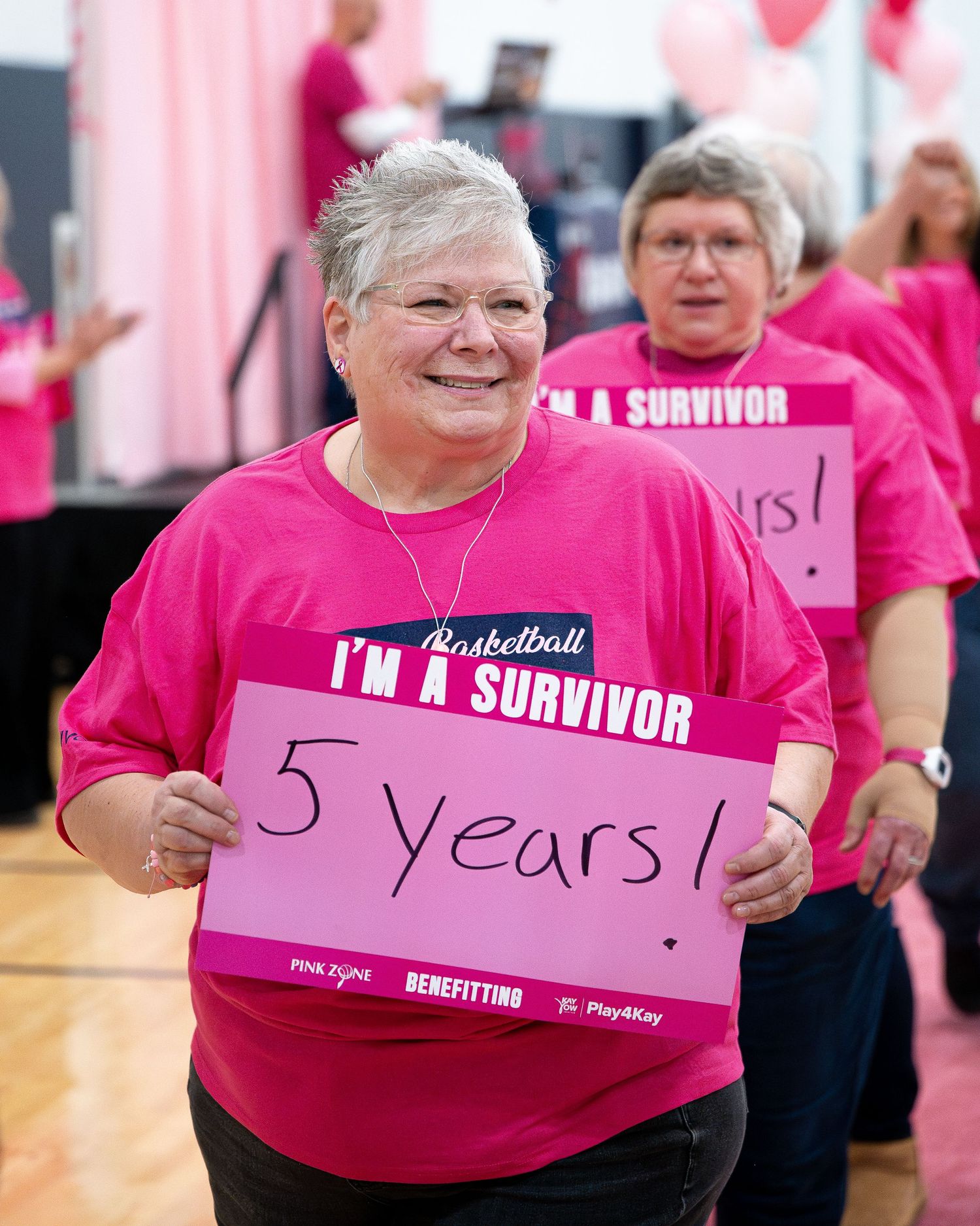 Cancer survivor wearing bright pink shirt proudly displays sign showing 5 years of survival.
