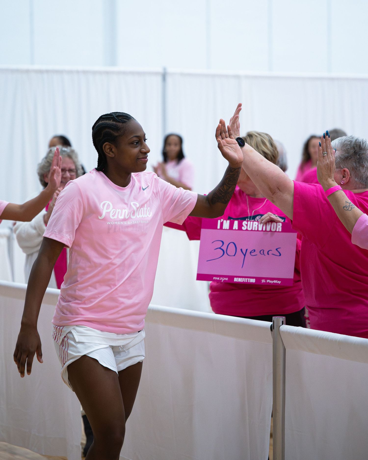 Athletes in pink shirts exchange high fives during breast cancer awareness celebration.