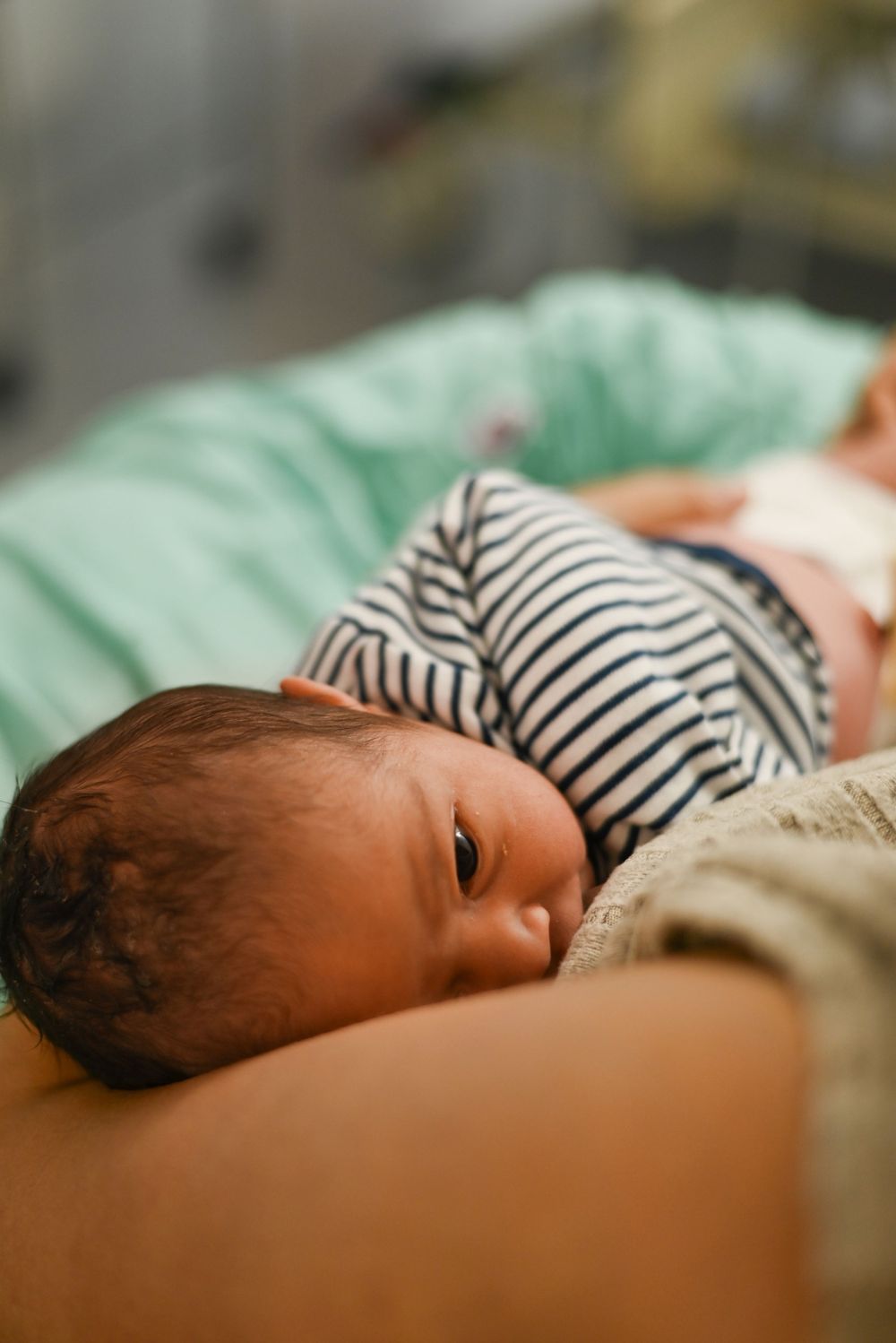 A newborn baby in striped clothing rests peacefully against a green cushioned surface.