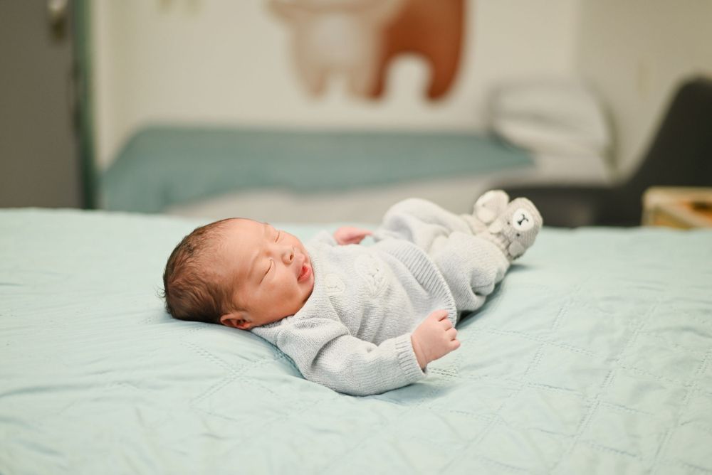 A tiny newborn baby wearing white sleeps peacefully on mint green bedding.