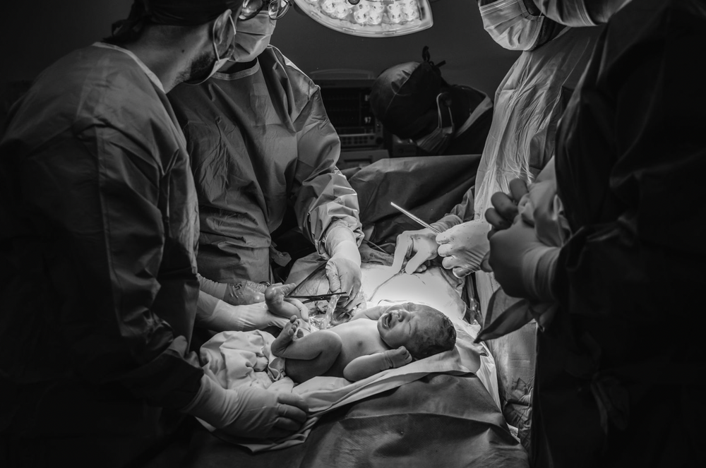 A dramatic black and white photograph captures medical professionals performing surgery in an operating room under bright lights.