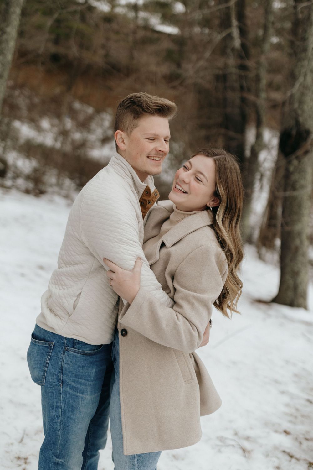 Joyful couple laughing while embracing outdoors in winter clothing.
