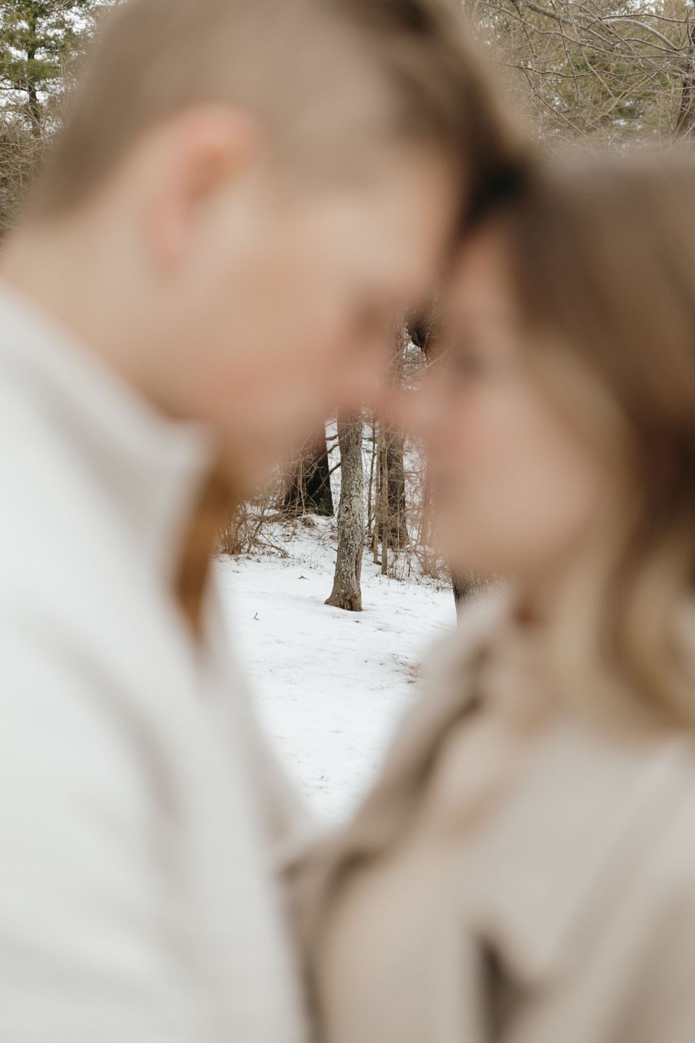 Artistic close-up photo with snowy forest backdrop visible between couple.