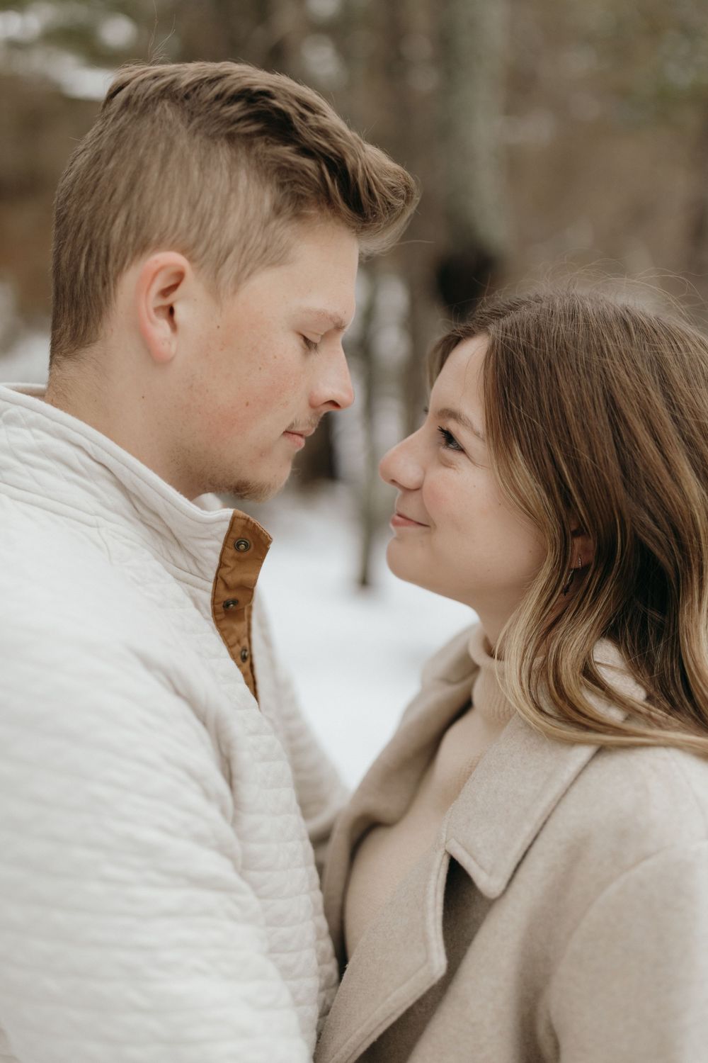 Close-up portrait of couple in cream and beige winter attire against snowy background.