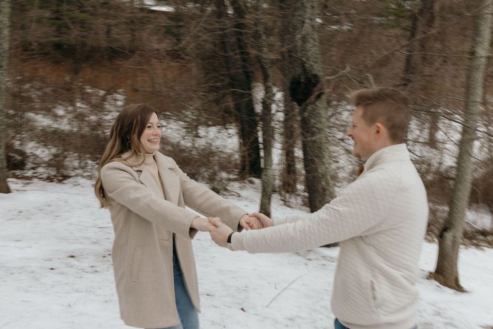 Couple dancing and spinning together in a snowy forest setting.