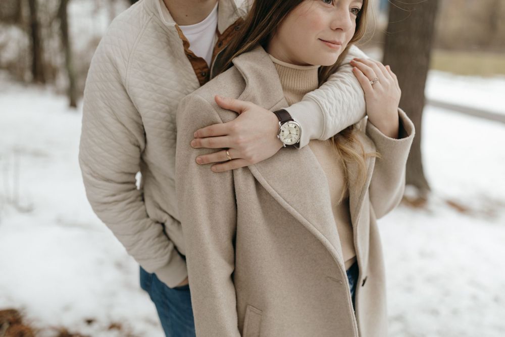 Couple in neutral winter clothing embracing in a tender moment among snow covered trees.