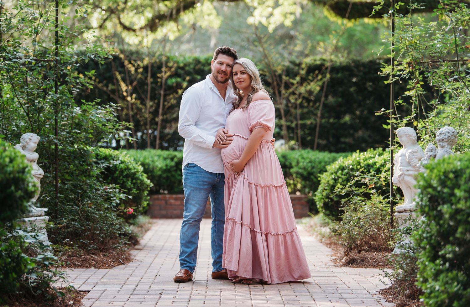 A couple shares a tender moment in a beautiful garden setting with a brick path and lush greenery surroundings.