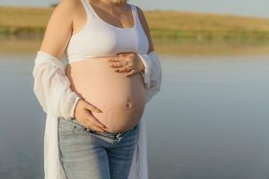 Close-up of pregnant belly with hands cradling bump against waterfront backdrop.