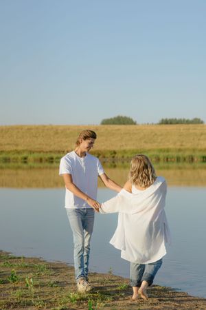 Couple holding hands while walking along lakeside path at sunset.