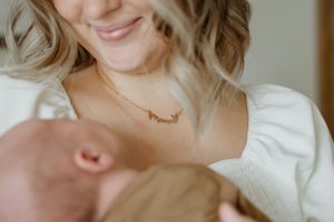 A tender moment between a newborn baby and parent wearing a delicate necklace.
