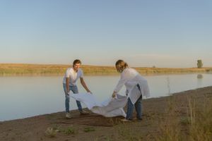Couple laying out a blanket together by a serene lake at golden hour.