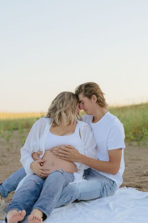 Expecting couple sharing an intimate moment on a blanket in a scenic field.