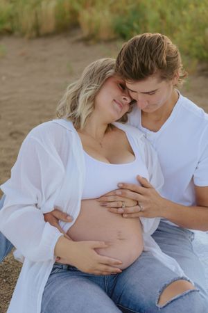 Couple embracing during maternity photoshoot in natural outdoor setting.