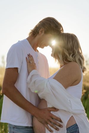 Intimate maternity moment captured between couple during golden sunset.