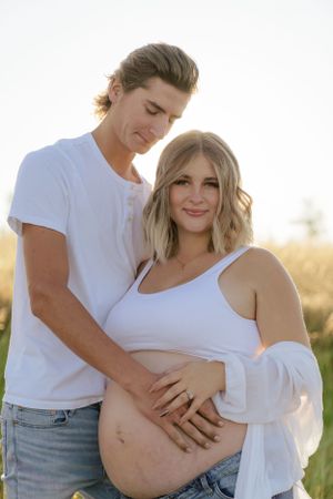 Maternity photoshoot in white outfits against golden field backdrop.