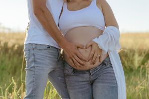 Close-up of hands cradling pregnant belly in casual outdoor setting.