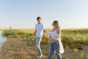 Couple walking together along waterside path during sunset maternity shoot.