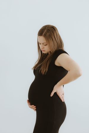 Side view of a pregnant figure wearing a fitted black dress against a white background.