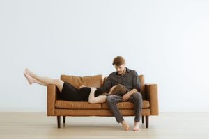 Couple lounging together on tan leather sofa in minimalist white room.
