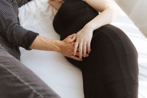 Close up of hands resting on pregnant belly while relaxing on white surface.