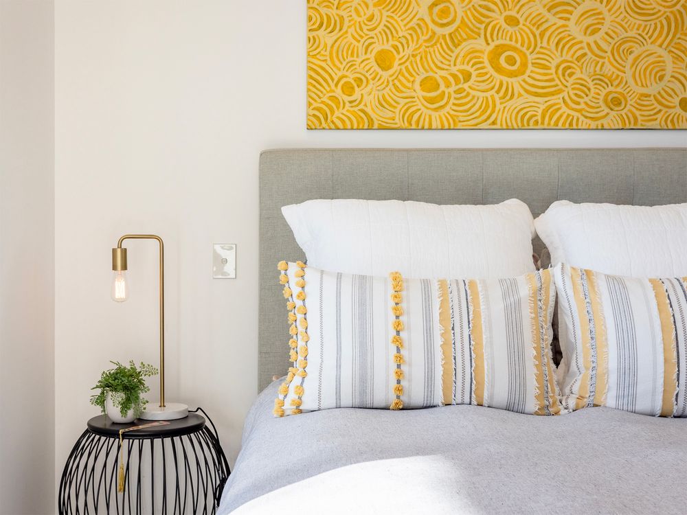 bedroom setting with yellow artwork blue bedspread and striped pillow cases