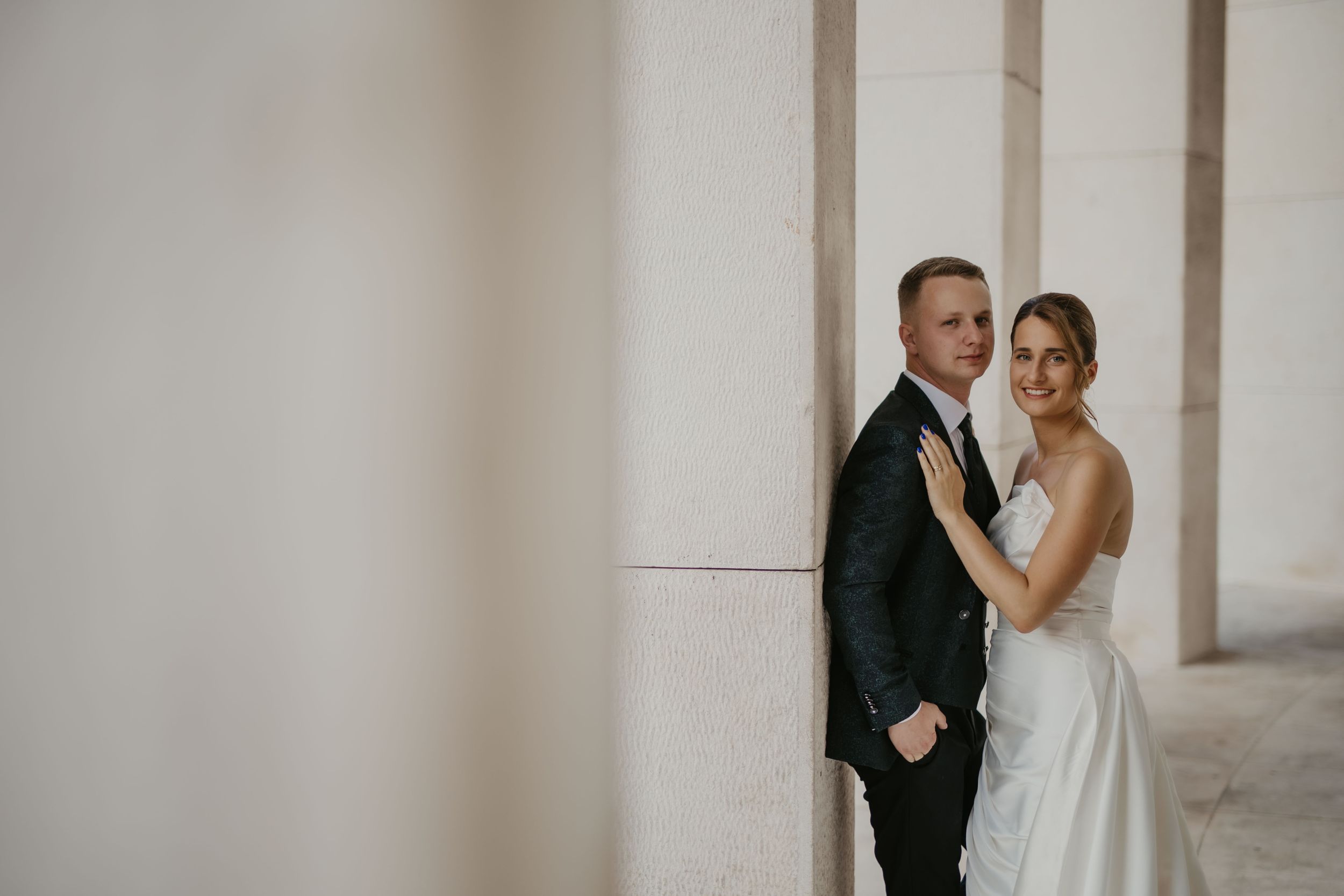 Elegant wedding portrait of a couple standing against white pillars in formal attire.