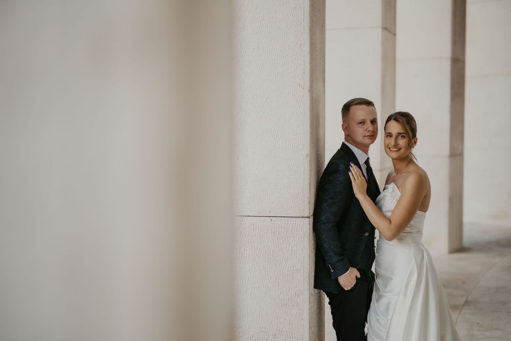 Elegant wedding portrait of a couple standing against white pillars in formal attire.