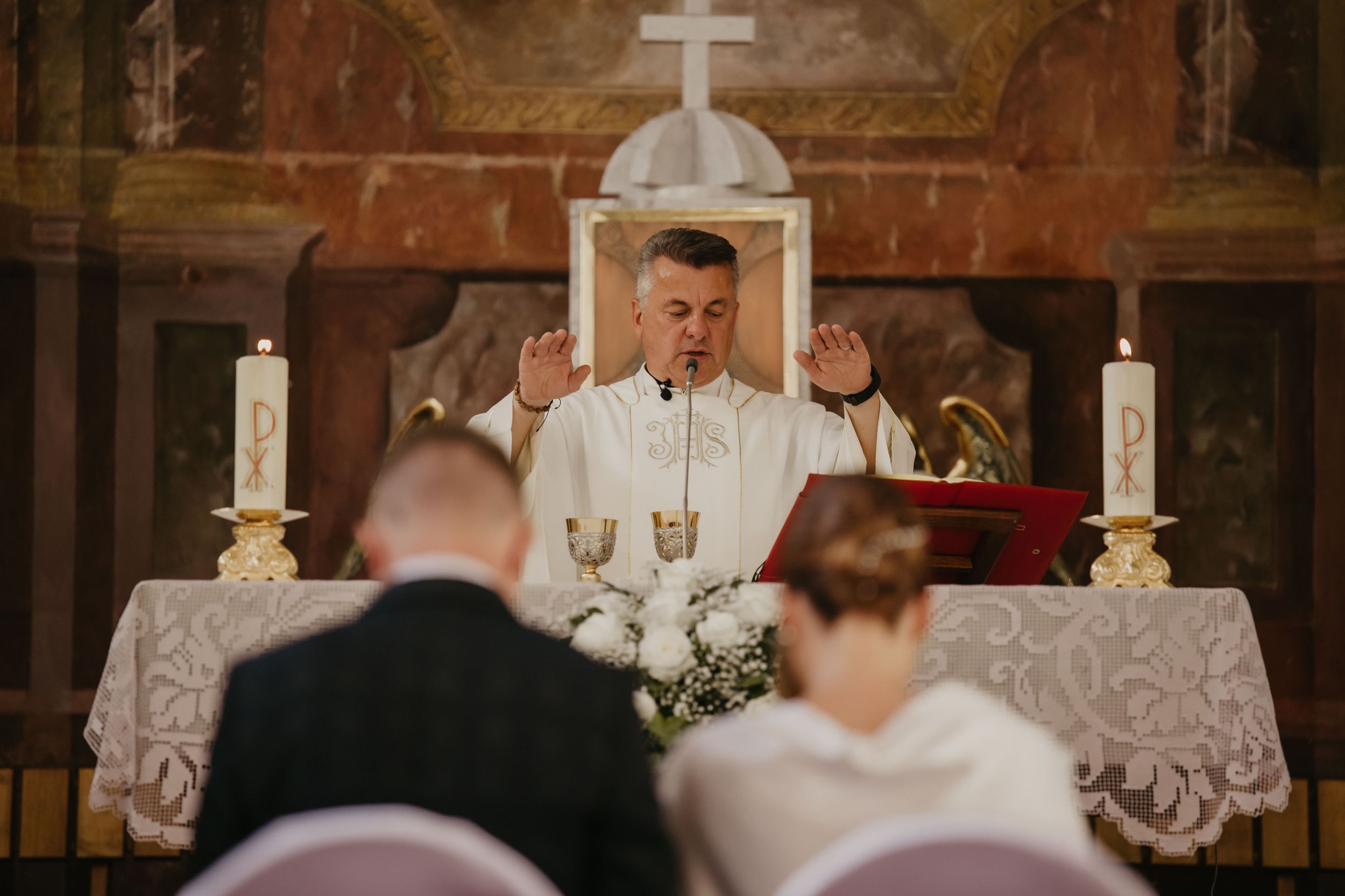 Catholic priest conducting a traditional wedding ceremony at an ornate altar with lit candles.