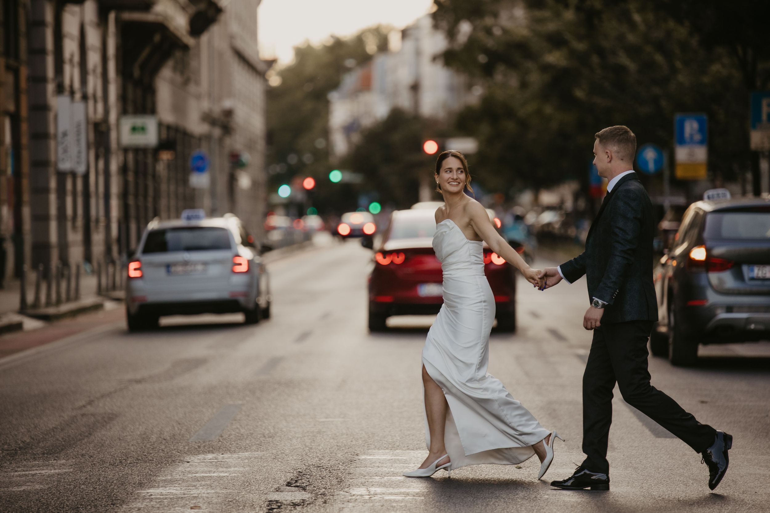 A playful wedding couple dances in the middle of a city street at dusk.