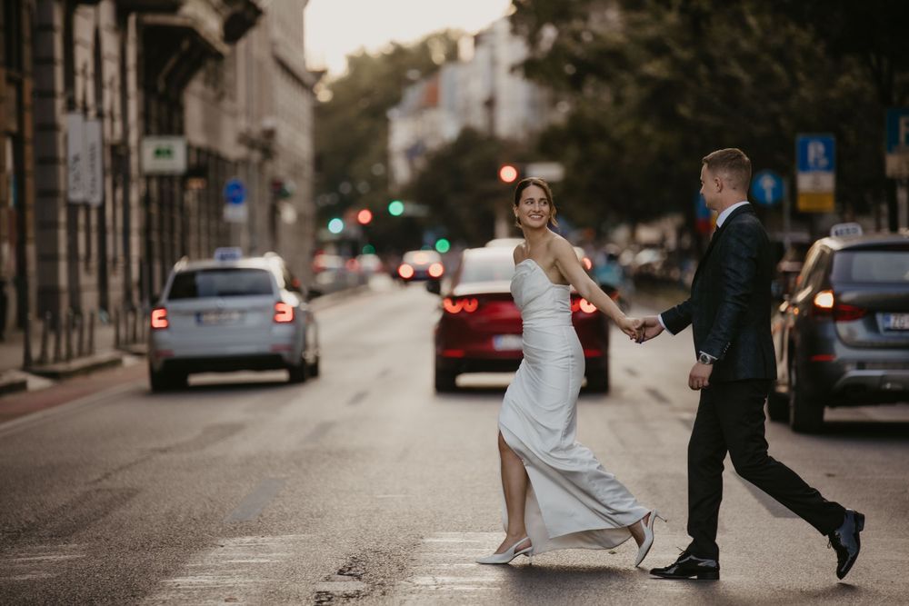 A playful wedding couple dances in the middle of a city street at dusk.